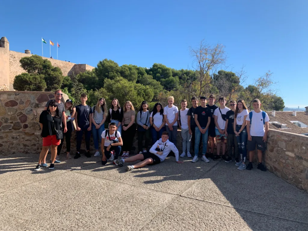 Die Gruppe sitzt vor einer Festungsanlage mit spanischer Flagge.